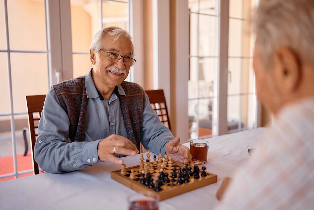 Senior man playing chess indoors with friend
